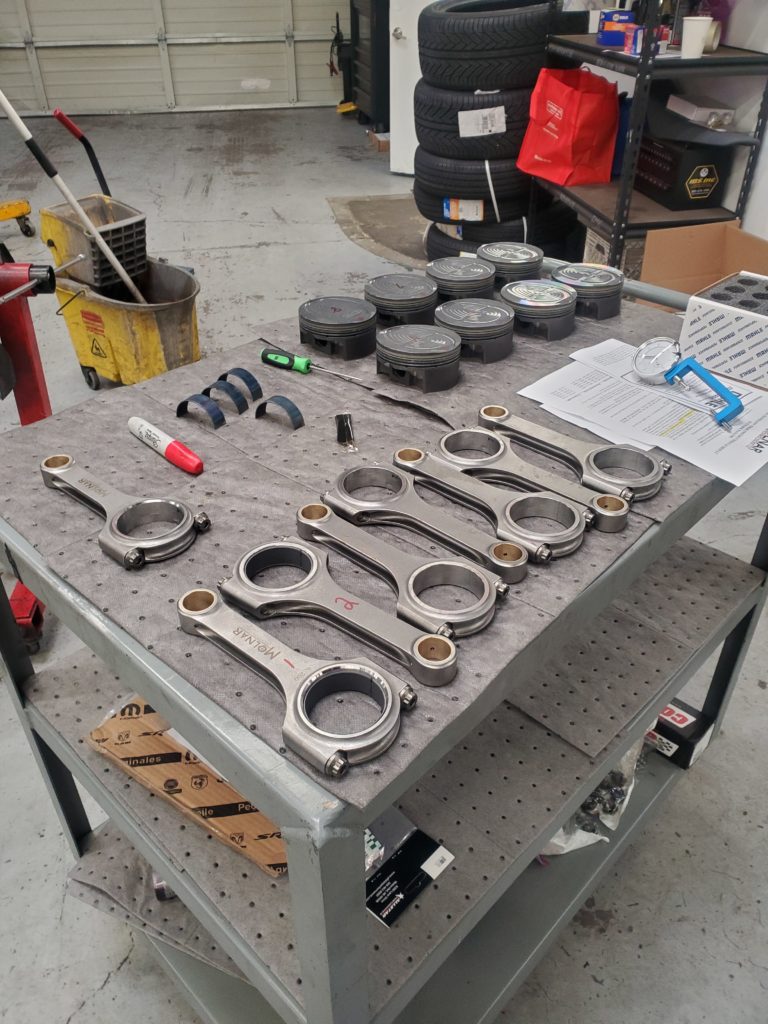 a set of connecting rods and matching pistons laid out on a workshop cart