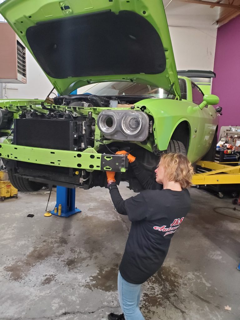 a J&S Automechanic working on a brightly colored, highlighter-green Dodge Challenger that is raised on a hydraulic lift