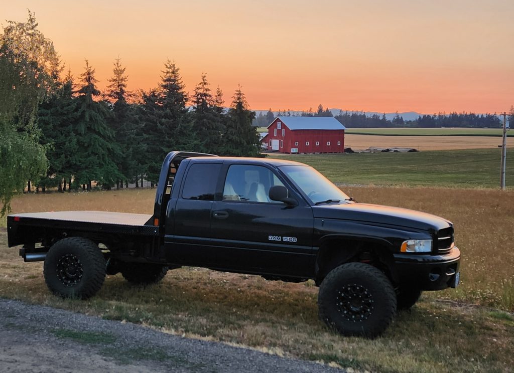 a lifted 2nd generation Dodge Ram (1994–2002) featuring an extended cab, a flatbed conversion, and rugged aftermarket wheels and mud tires