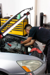 J&S Automotive technician performing engine maintenance on a silver sedan