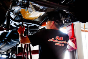 J&S Automotive technician performing automotive repair on a vehicle lifted on a hydraulic hois